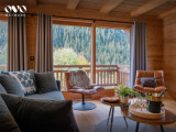 Salon avec ses canapés, fauteuils et grande baie vitrée donnant accès au balcon et vue sur les montagnes