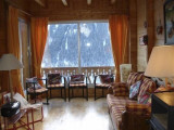 Salon avec grande baie vitrée donnant accès au balcon, vue sur les montagnes, nombreux fauteuils et un canapé