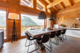 Salle à manger avec une grande table, grandes baies vitrées offrant une vue panoramique sur les montagnes